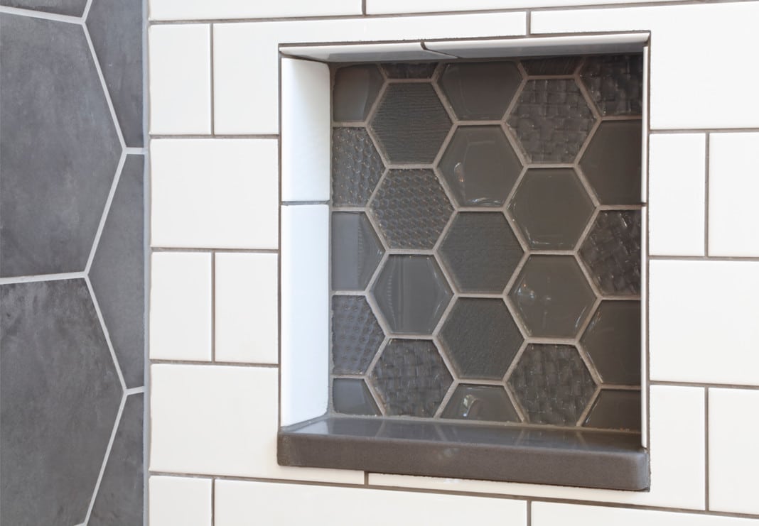 Matte grey octagon tile on the left wall of the shower, with grey glass octagon tile in various textures inside the shower niches